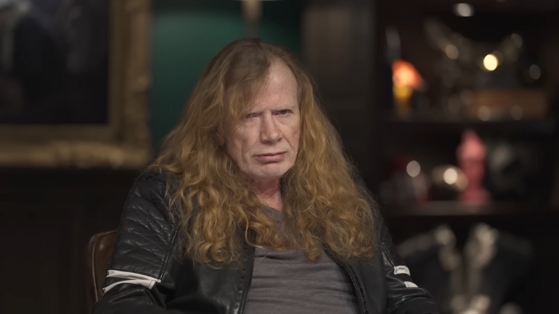 Dave Mustaine seated indoors with a serious expression, wearing a black leather jacket