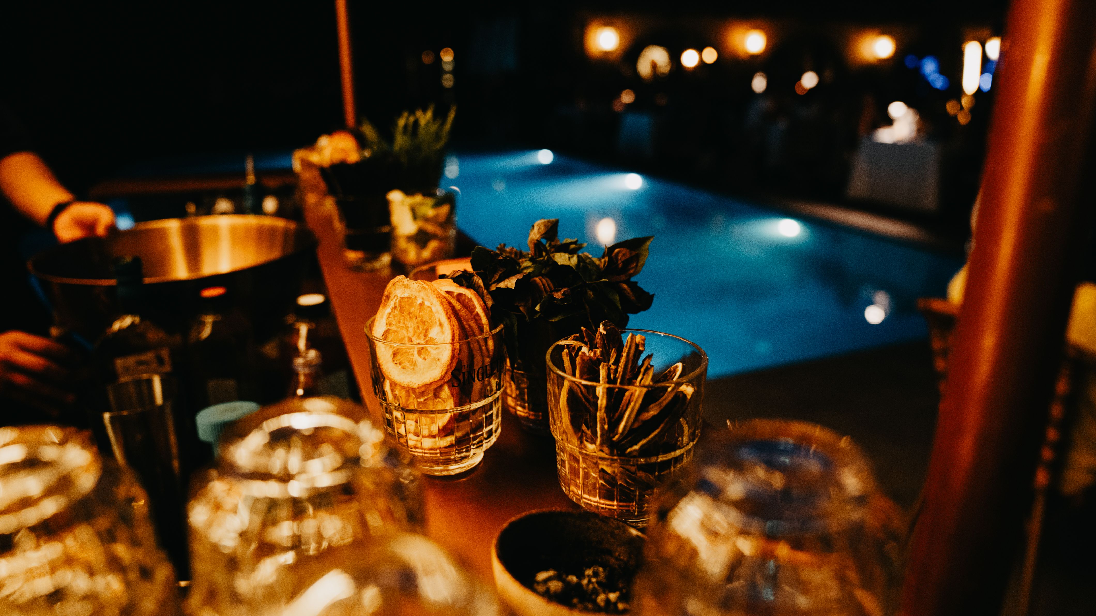 Stylish poolside bar setup at night with fresh garnishes and warm ambient lighting