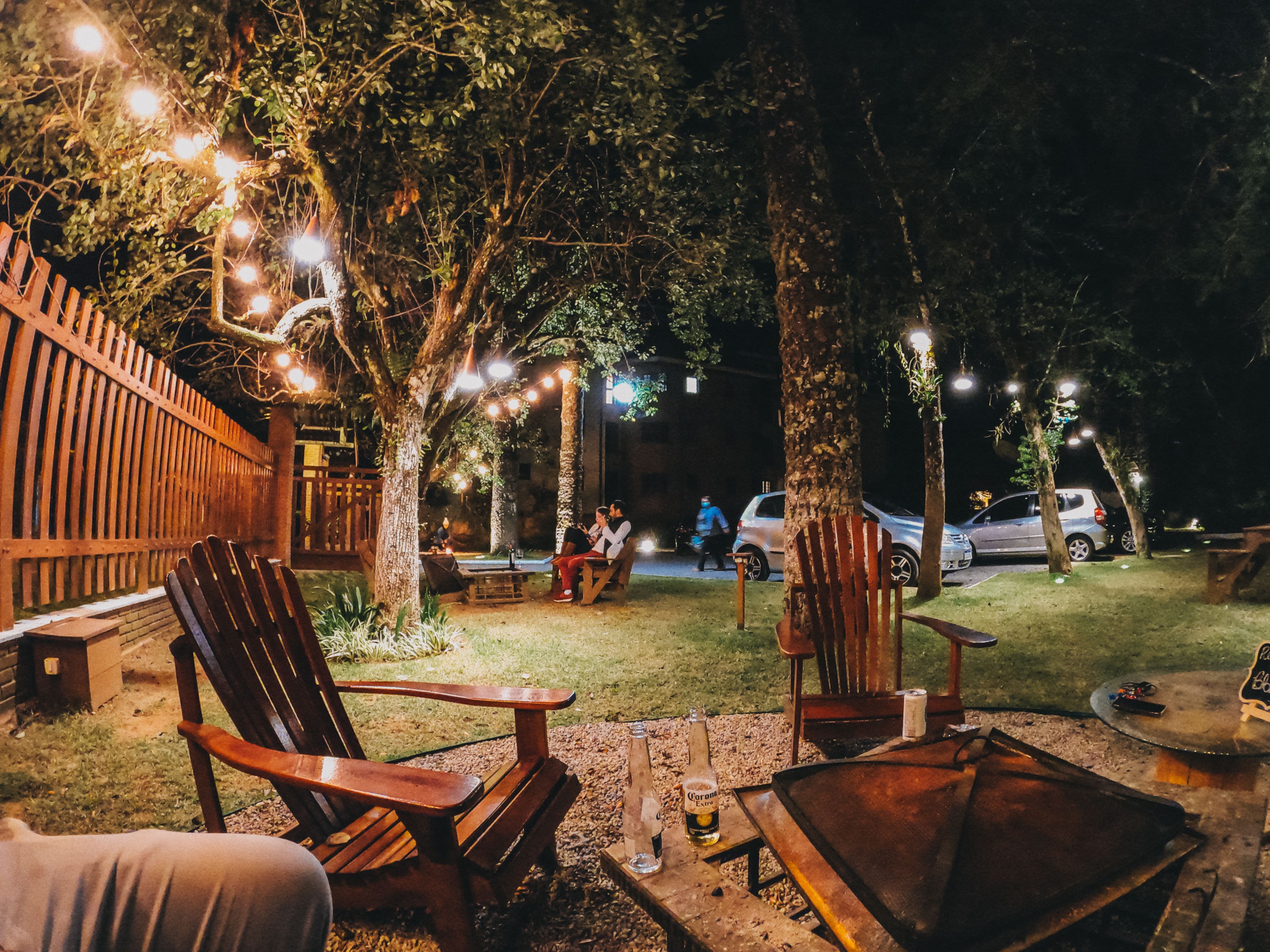 People relaxing on wooden chairs in a backyard with garlands in the trees at night